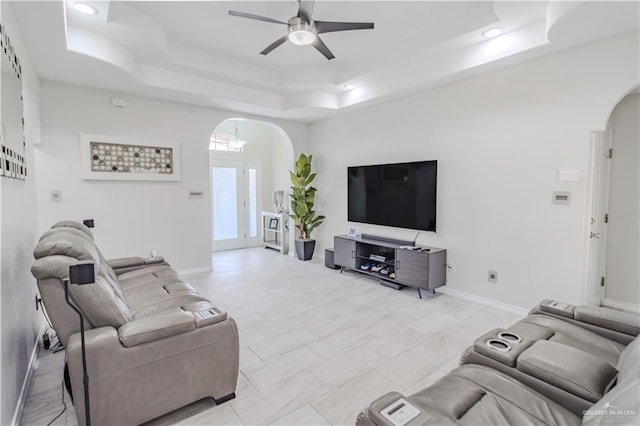 living area with baseboards, arched walkways, ceiling fan, a tray ceiling, and recessed lighting