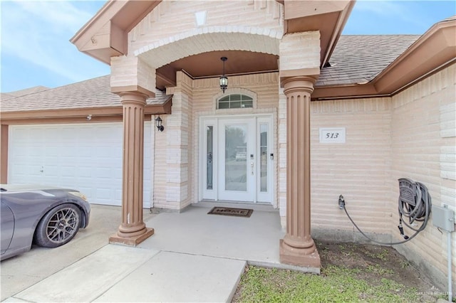 doorway to property with an attached garage, brick siding, and roof with shingles