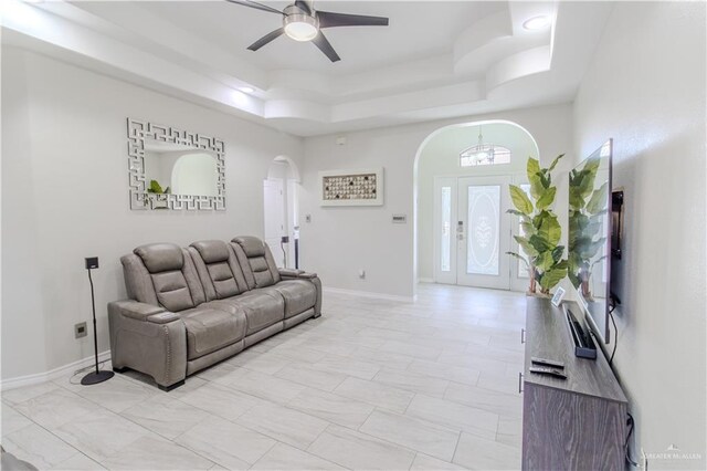 living room featuring a ceiling fan, baseboards, arched walkways, and a tray ceiling