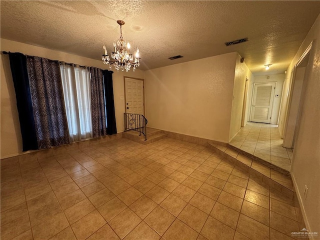 tiled spare room with a textured ceiling and a chandelier