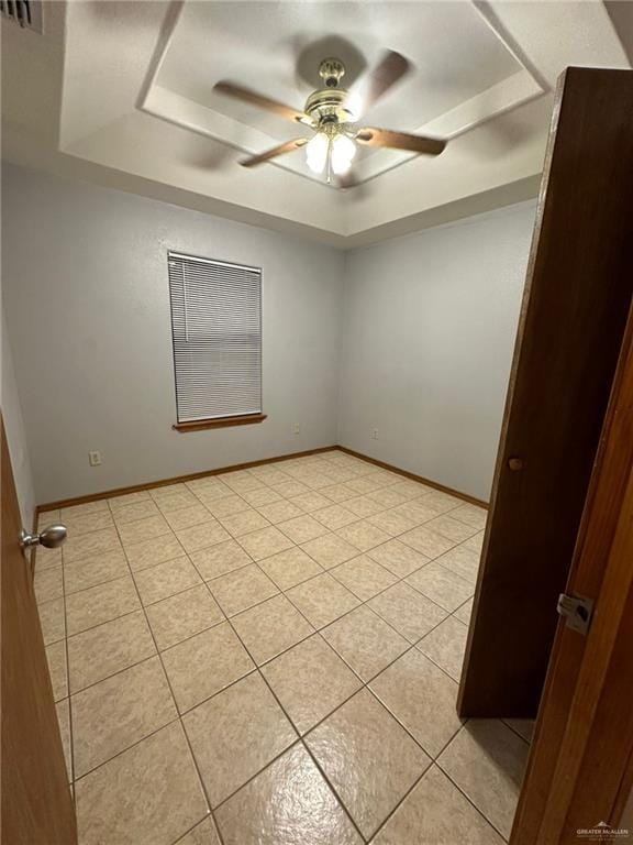 unfurnished room featuring a raised ceiling, ceiling fan, and light tile patterned flooring