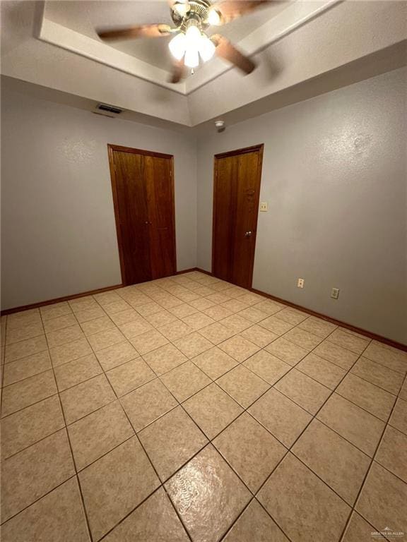 tiled spare room with a raised ceiling and ceiling fan