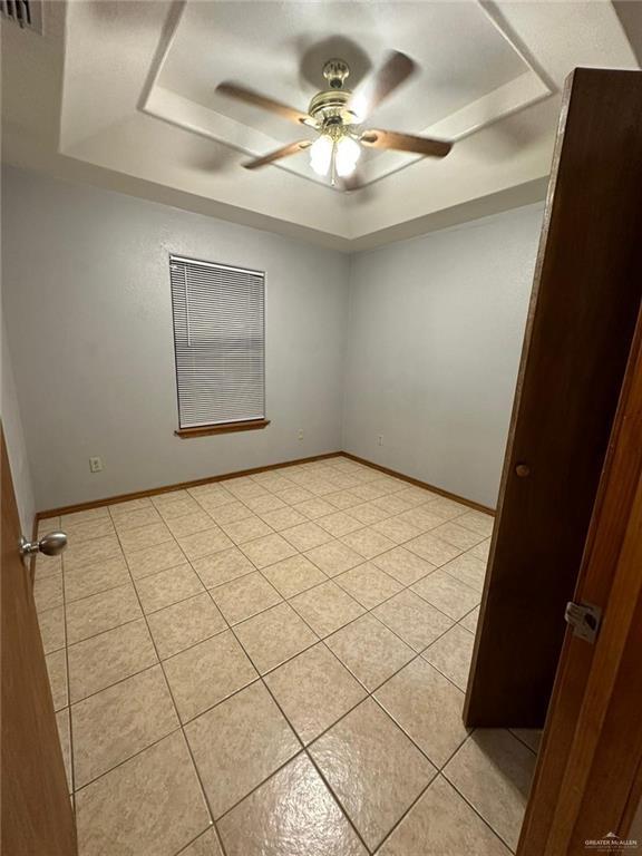 tiled empty room with a raised ceiling and ceiling fan