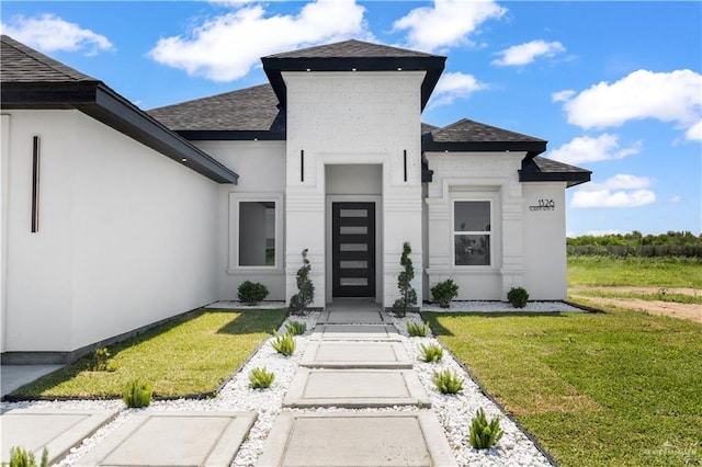 1326 S 9th St, Alamo, TX 78516 - view of exterior entry featuring a yard, a shingled roof, and stucco siding
