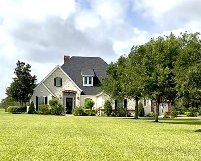 1630 E California Rd, Los Fresnos, TX 78566 - french country home featuring a chimney, stone siding, and a front yard
