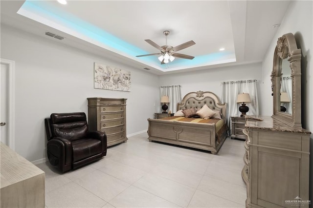 bedroom with ceiling fan, a tray ceiling, visible vents, and baseboards