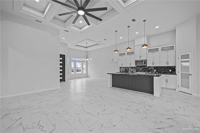 kitchen with decorative light fixtures, white cabinetry, open floor plan, stainless steel microwave, and glass insert cabinets