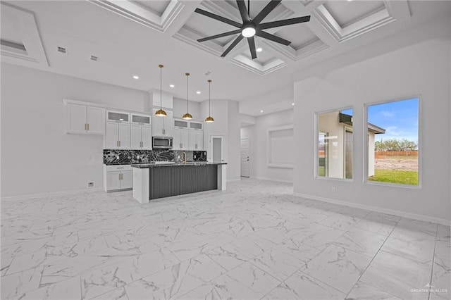 kitchen with decorative light fixtures, a center island with sink, stainless steel microwave, open floor plan, and white cabinetry