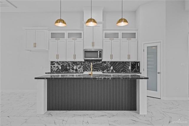 kitchen with hanging light fixtures, stainless steel microwave, glass insert cabinets, and white cabinets