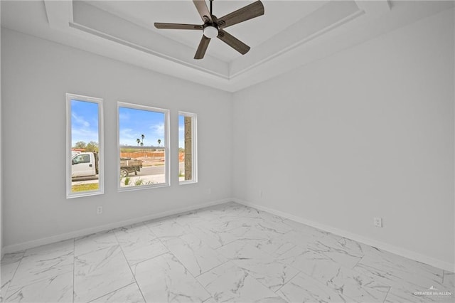 spare room featuring a tray ceiling, marble finish floor, and baseboards