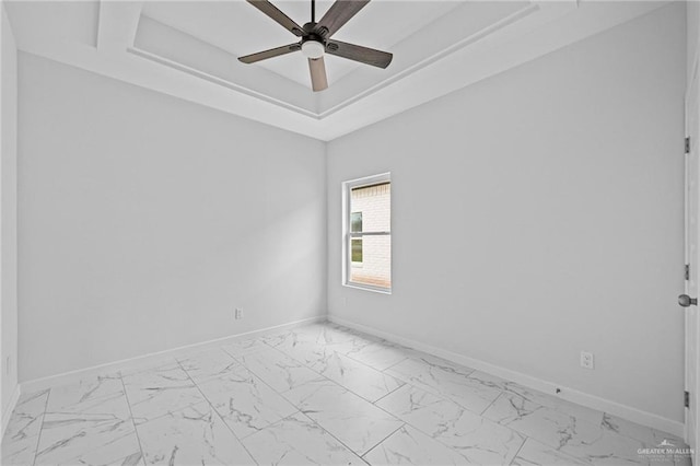 unfurnished room with a ceiling fan, a raised ceiling, marble finish floor, and baseboards