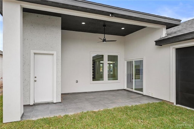 view of exterior entry featuring ceiling fan, a patio, a yard, and stucco siding