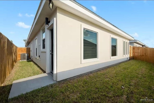 view of side of home featuring central air condition unit, a fenced backyard, a yard, and stucco siding