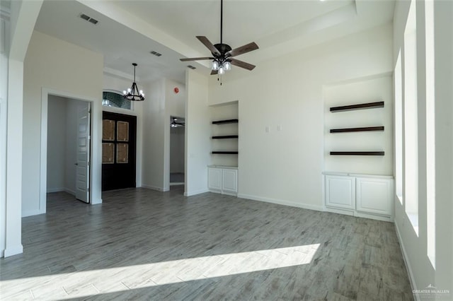 unfurnished living room with built in features, light hardwood / wood-style floors, and ceiling fan with notable chandelier