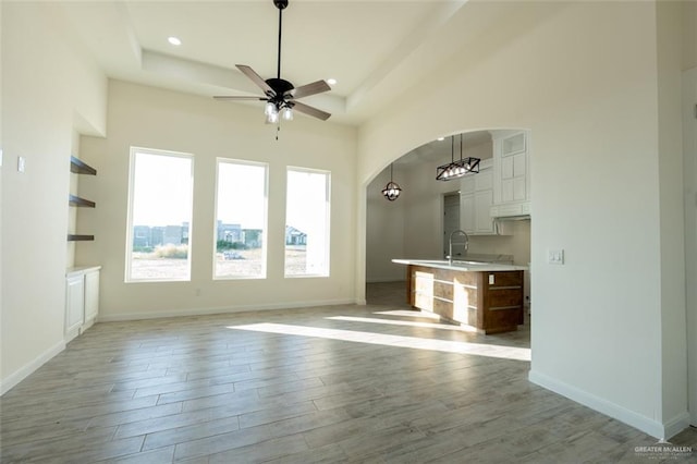 unfurnished living room with ceiling fan, a raised ceiling, sink, and a high ceiling