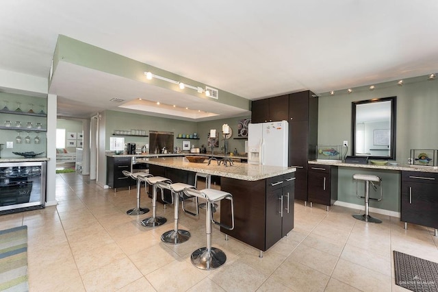 kitchen featuring light stone countertops, a kitchen island, white fridge with ice dispenser, and a breakfast bar area