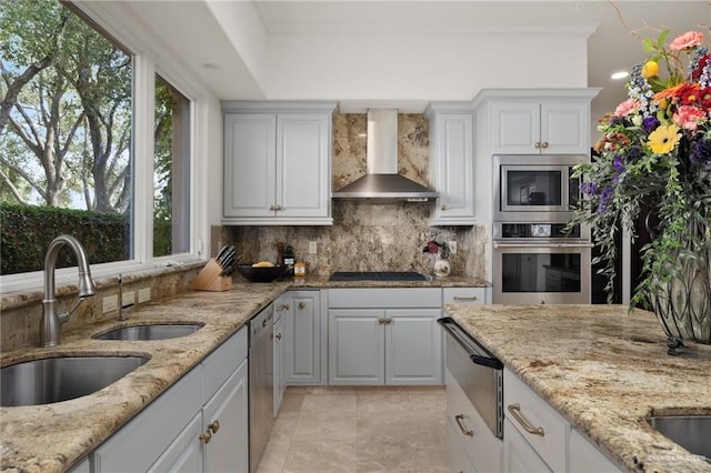 kitchen featuring decorative backsplash, appliances with stainless steel finishes, light stone countertops, wall chimney range hood, and a sink