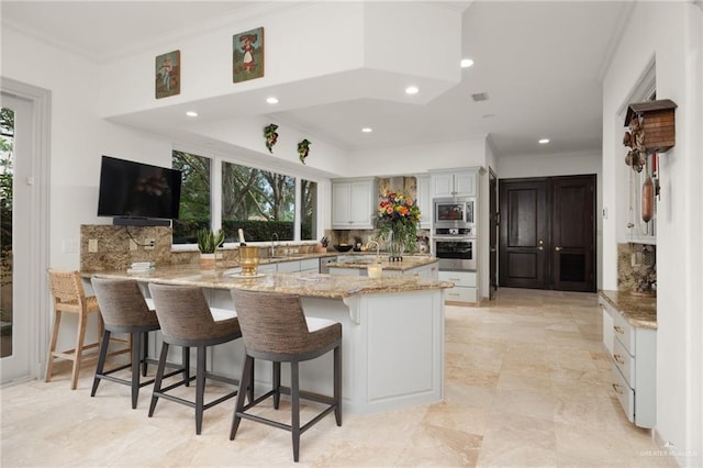 kitchen with a breakfast bar area, appliances with stainless steel finishes, white cabinetry, light stone countertops, and a peninsula