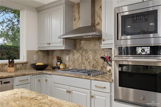 kitchen with stainless steel appliances, wall chimney range hood, white cabinetry, and tasteful backsplash