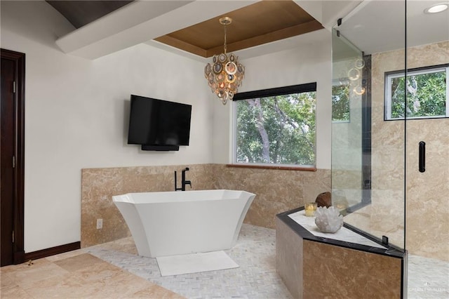 full bathroom featuring tile walls, a shower, a soaking tub, a tray ceiling, and an inviting chandelier