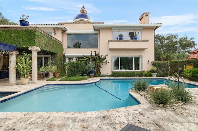 rear view of property featuring a fenced in pool, a patio area, a chimney, and stucco siding