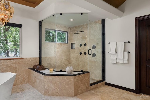 bathroom with a notable chandelier, tile walls, a soaking tub, a stall shower, and baseboards