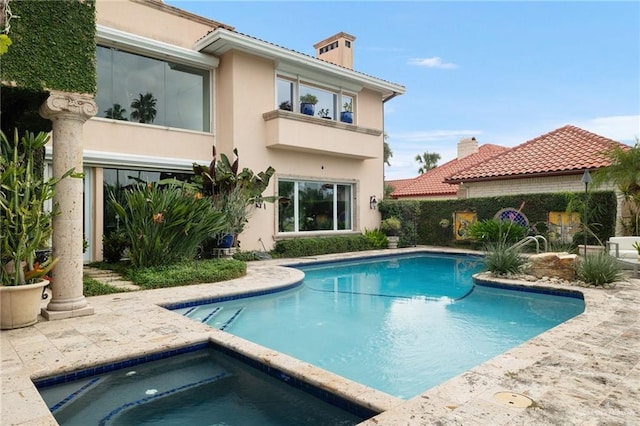 rear view of house featuring an in ground hot tub, an outdoor pool, and stucco siding