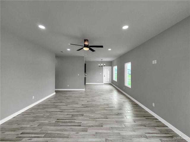 unfurnished living room featuring ceiling fan with notable chandelier and light hardwood / wood-style flooring