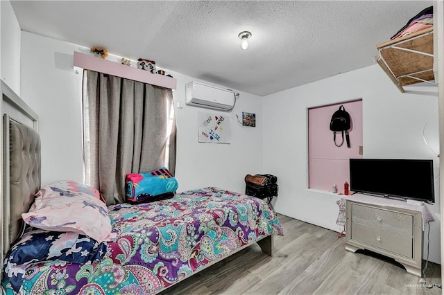 bedroom featuring a textured ceiling, a wall unit AC, and light wood-type flooring