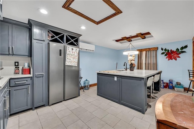 kitchen with pendant lighting, gray cabinetry, stainless steel refrigerator, a center island with sink, and a wall mounted air conditioner