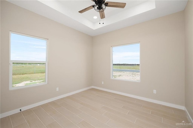 empty room with a tray ceiling, a wealth of natural light, ceiling fan, and light hardwood / wood-style floors