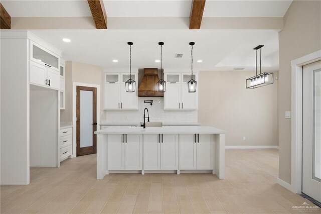 kitchen featuring white cabinetry, a kitchen island with sink, decorative light fixtures, and custom exhaust hood