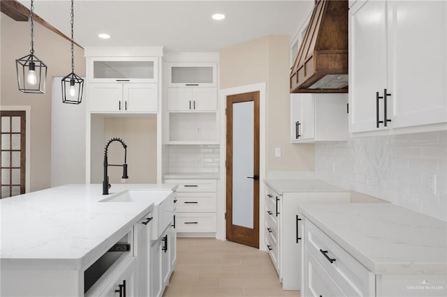 kitchen with white cabinetry, a center island with sink, hanging light fixtures, and light stone counters