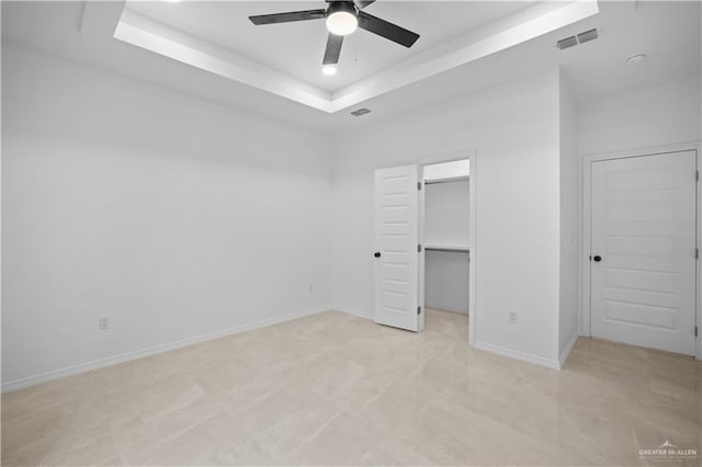 unfurnished bedroom featuring a tray ceiling, a walk in closet, a closet, and ceiling fan