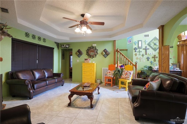 living room with a tray ceiling, ceiling fan, light tile patterned flooring, and a textured ceiling