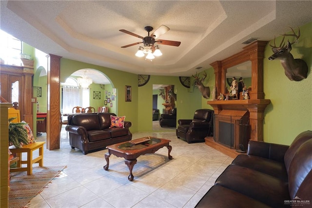 living room with ceiling fan with notable chandelier, light tile patterned floors, a large fireplace, and a tray ceiling