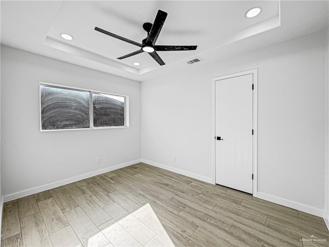 spare room with light hardwood / wood-style flooring, a raised ceiling, and ceiling fan