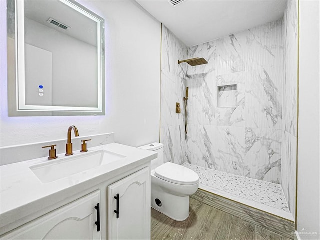 bathroom with a tile shower, toilet, vanity, and hardwood / wood-style flooring