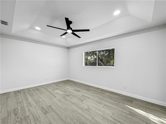 spare room featuring a tray ceiling, ceiling fan, and light hardwood / wood-style floors