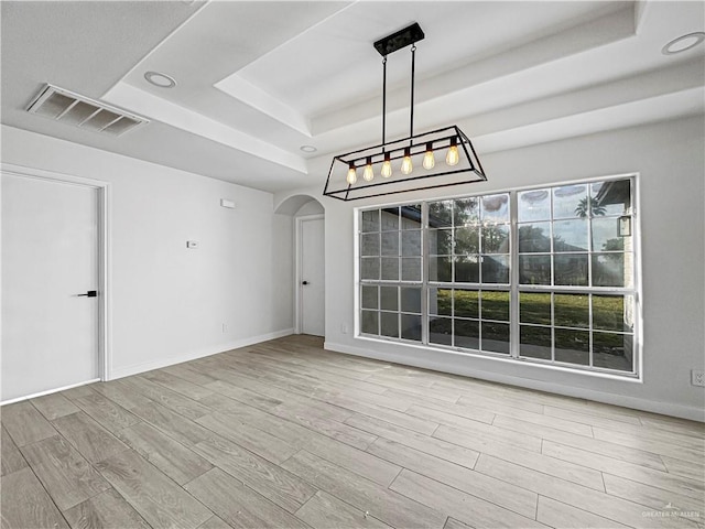 unfurnished dining area featuring light hardwood / wood-style floors and a tray ceiling