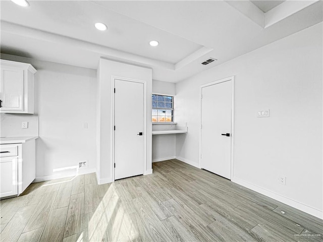 empty room with a raised ceiling and light hardwood / wood-style flooring