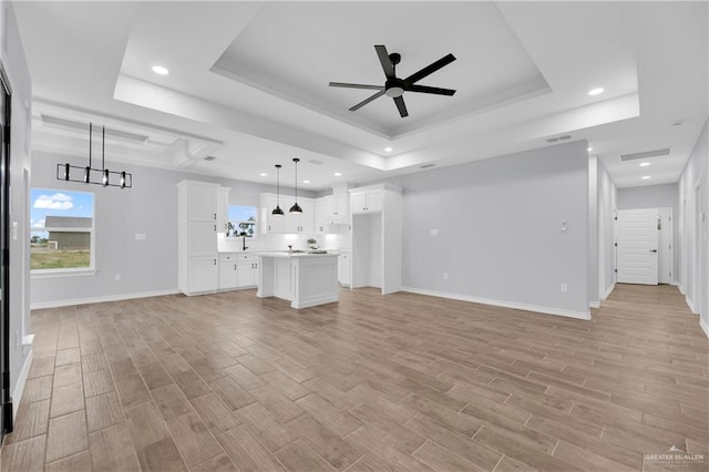 unfurnished living room with a raised ceiling, light hardwood / wood-style floors, and ceiling fan with notable chandelier