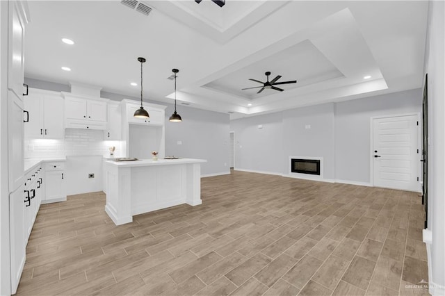 kitchen with a center island with sink, light wood-type flooring, white cabinetry, and a tray ceiling