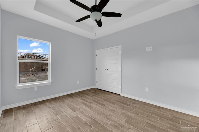 unfurnished bedroom with ceiling fan, a closet, light wood-type flooring, and a tray ceiling