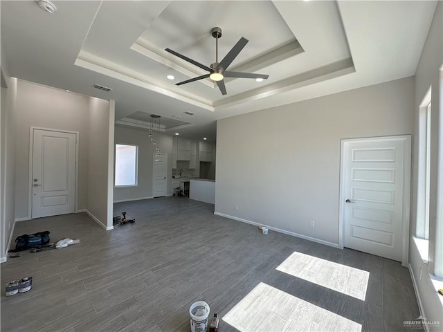 unfurnished living room with visible vents, baseboards, a tray ceiling, and wood finished floors