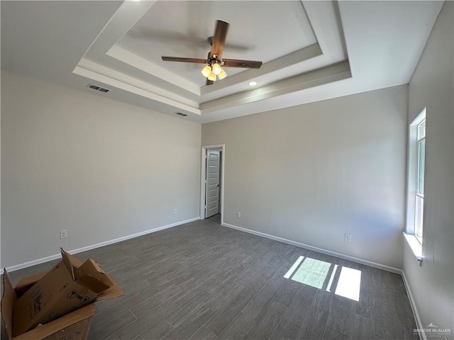 spare room featuring visible vents, dark wood-type flooring, a tray ceiling, baseboards, and ceiling fan