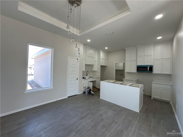 kitchen featuring visible vents, a sink, white cabinets, a raised ceiling, and stainless steel microwave