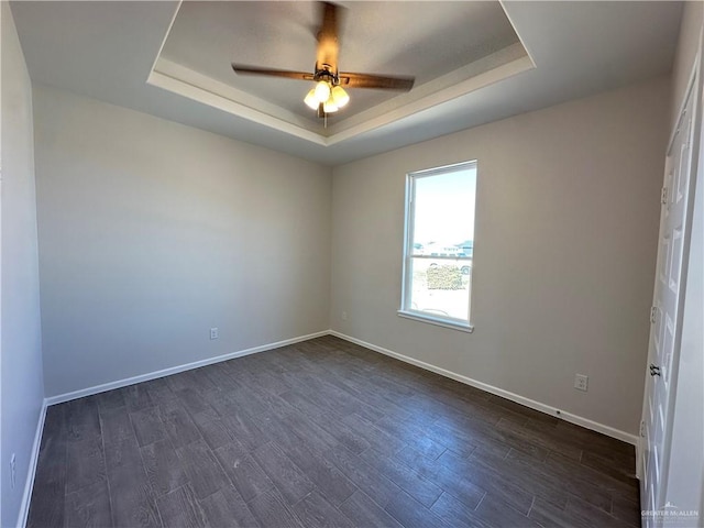 spare room with dark wood finished floors, a ceiling fan, a raised ceiling, and baseboards