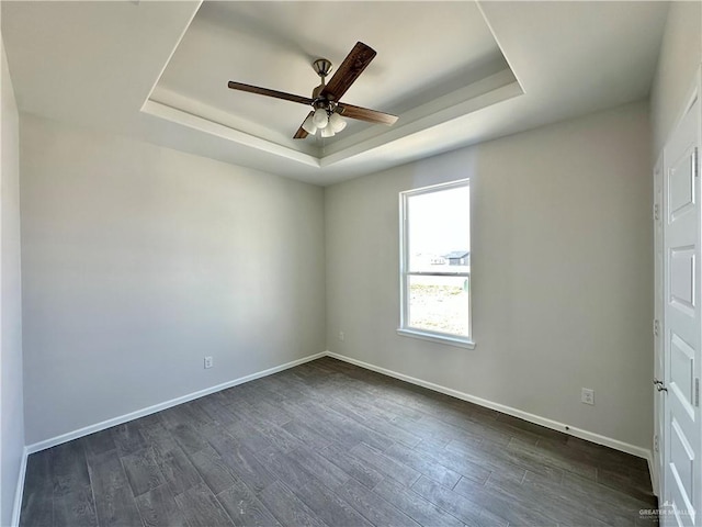 empty room with a raised ceiling, dark wood-style floors, and baseboards