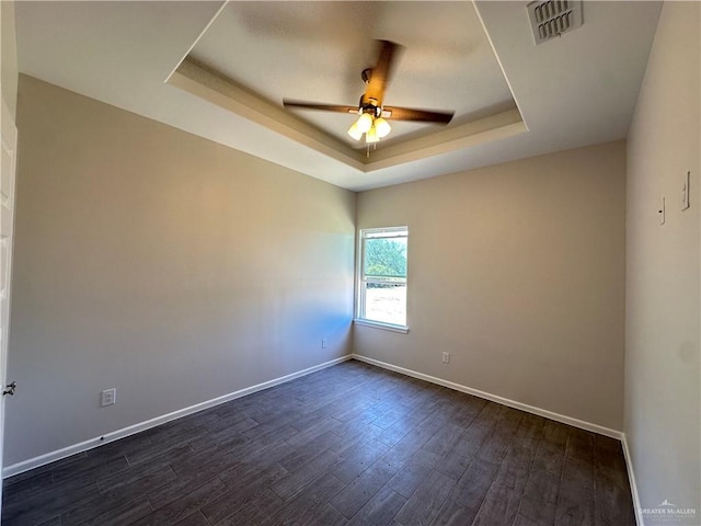 empty room featuring dark wood finished floors, a tray ceiling, baseboards, and visible vents